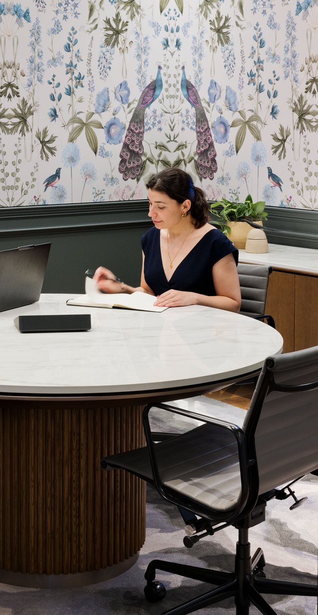 Two colleagues working at a round table in front of a botanical mural